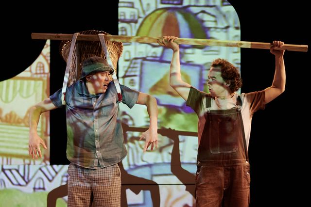 Performer holding up a stick while another performer is being pulled up by his attached backpack