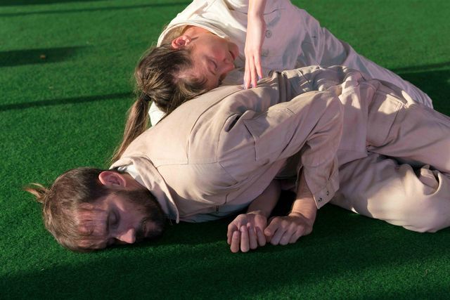 Two performers lying on plastic lawn