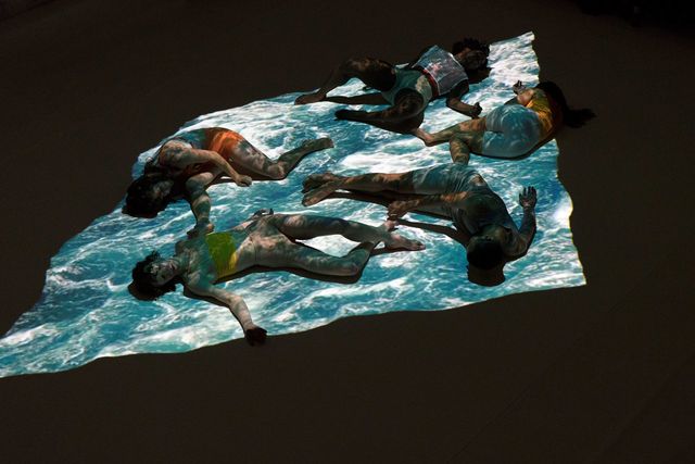 Five performers lying on a projected surface