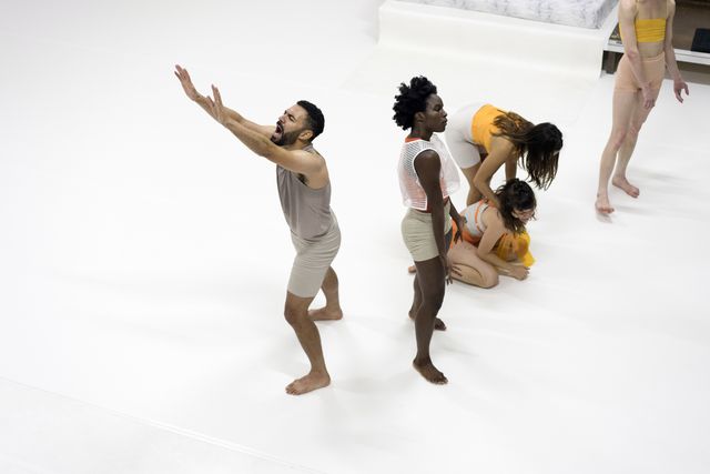 One performer screaming and reaching out his arms while more performers are facing away from him