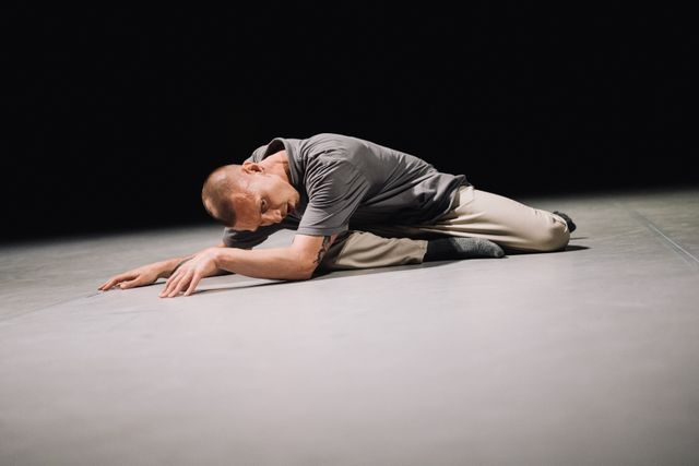 Male performer kneeling on stage with his hands stretched forwards
