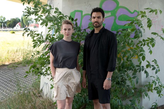 The two artists Cindy Hammer and Joseph Hernandez portrayed in front of a bush under a bridge