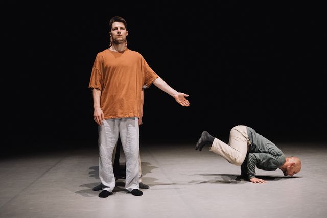 Male performer pointing at another male dancer who is performing a pose on his hands