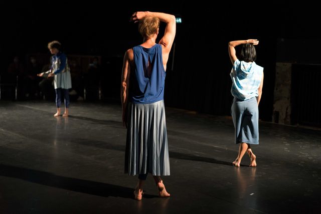 Three dancers in blue outfits standing up straight, hands facing different directions