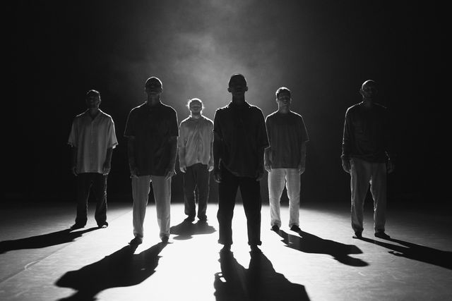 Group of male performers standing separately with dramatic backlight